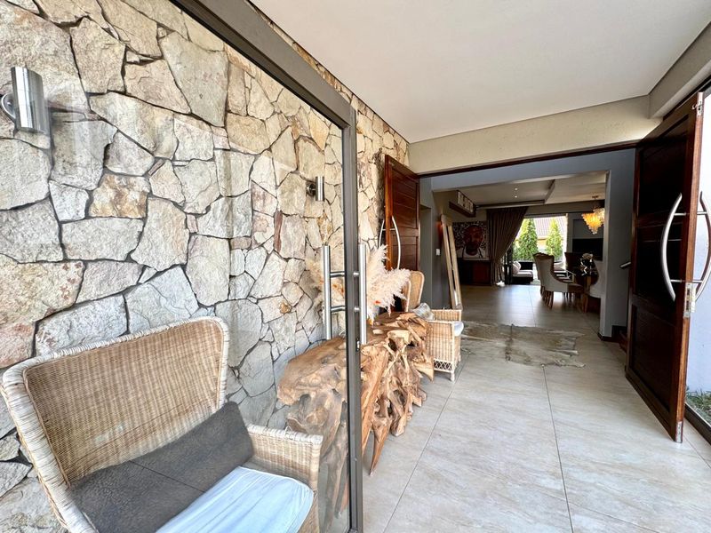 A welcoming entrance area featuring a striking natural stone feature wall, large format floor tiles, and double wooden doors leading into the main living space.