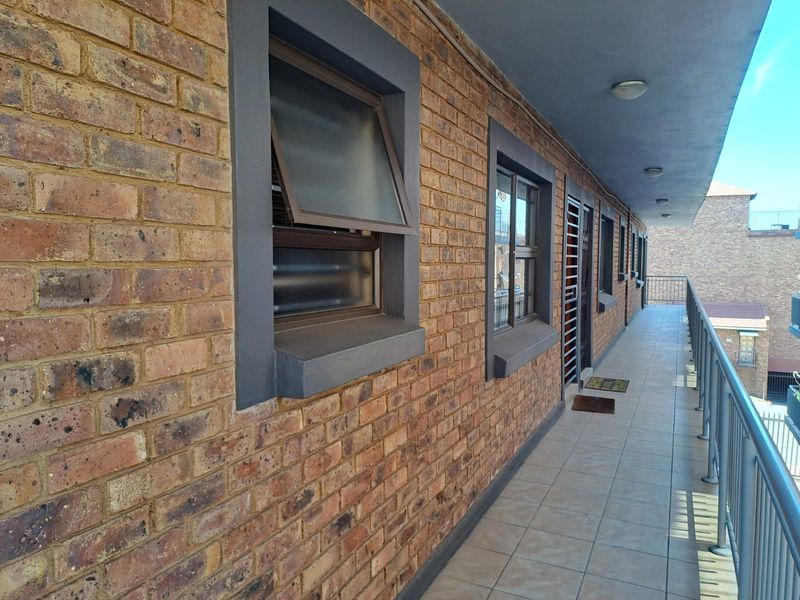 A covered balcony featuring exposed brick walls, tiled flooring, and metal safety railings, providing an outdoor walkway along the townhouse exterior.