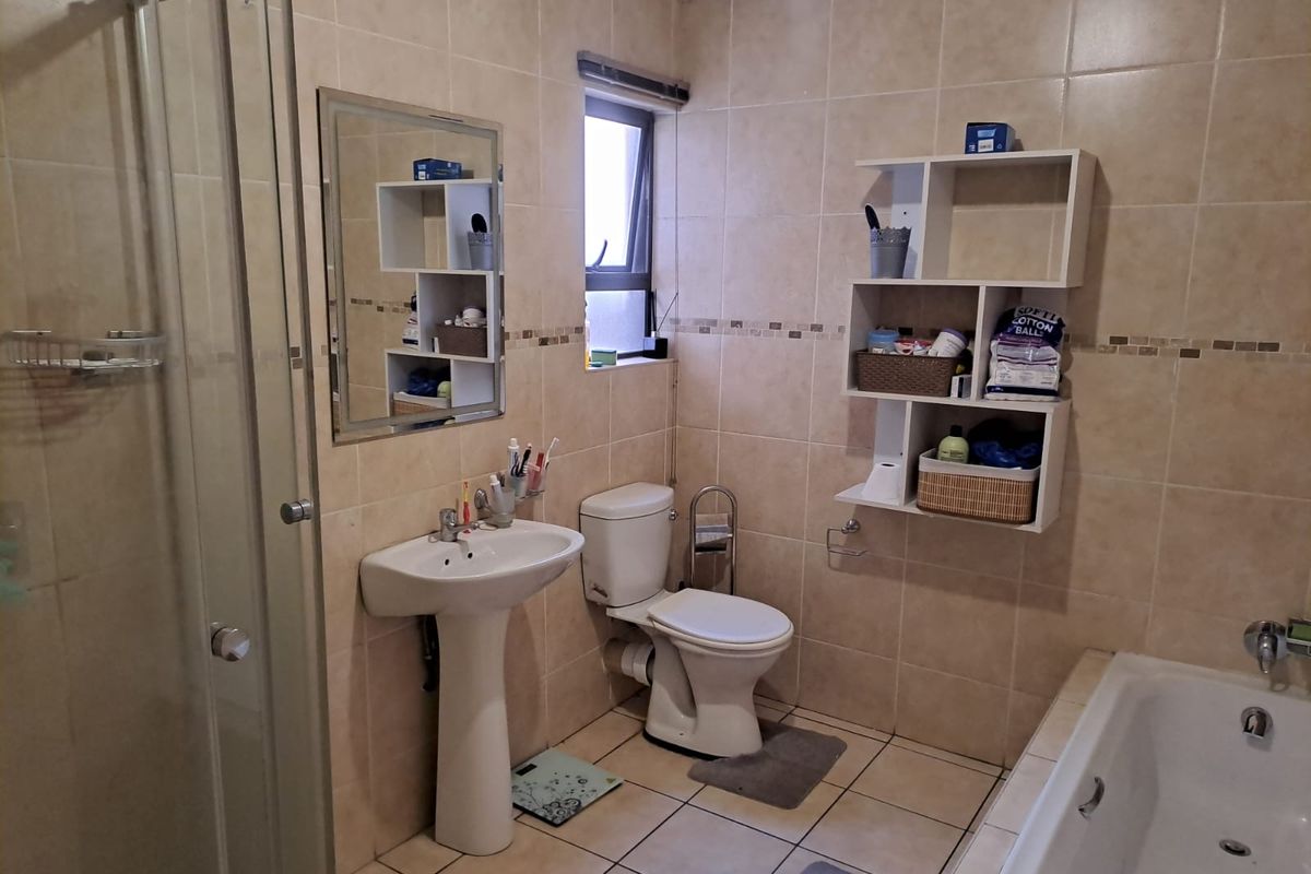 A functional bathroom featuring a pedestal basin, toilet, shower enclosure, and bathtub with neutral wall and floor tiling.
