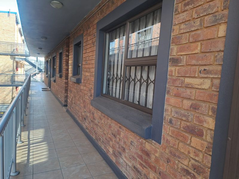 A covered exterior balcony featuring exposed brickwork, tiled flooring, and secure metal balustrades, providing access to the townhouse unit.