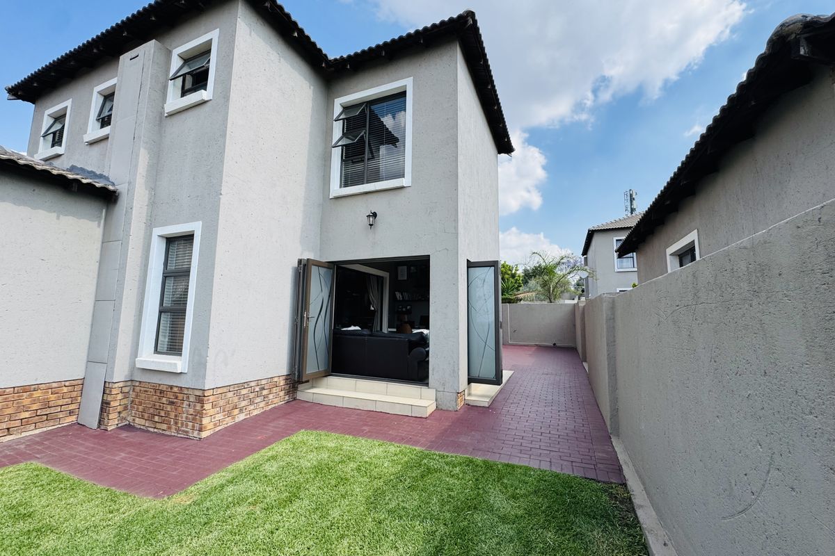 Rear view of the townhouse featuring a paved patio area, small lawn, and double-story exterior facade with tiled roof.
