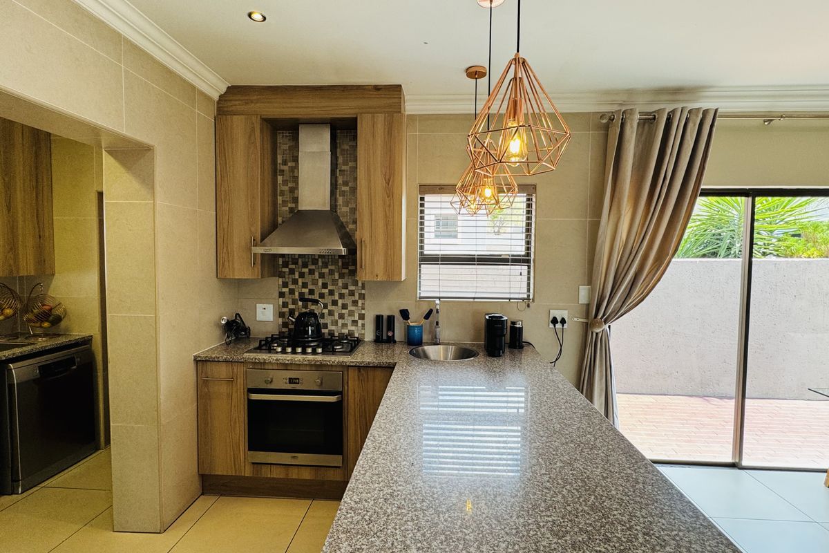 Modern kitchen featuring granite countertops, built-in oven, gas hob, extractor fan, and a breakfast bar, with direct access to an outdoor patio area.