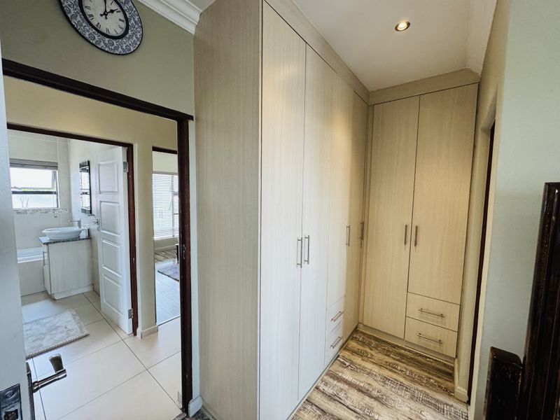 A well-maintained dressing area featuring built-in light wood cabinetry with ample storage, leading into an adjacent bathroom.