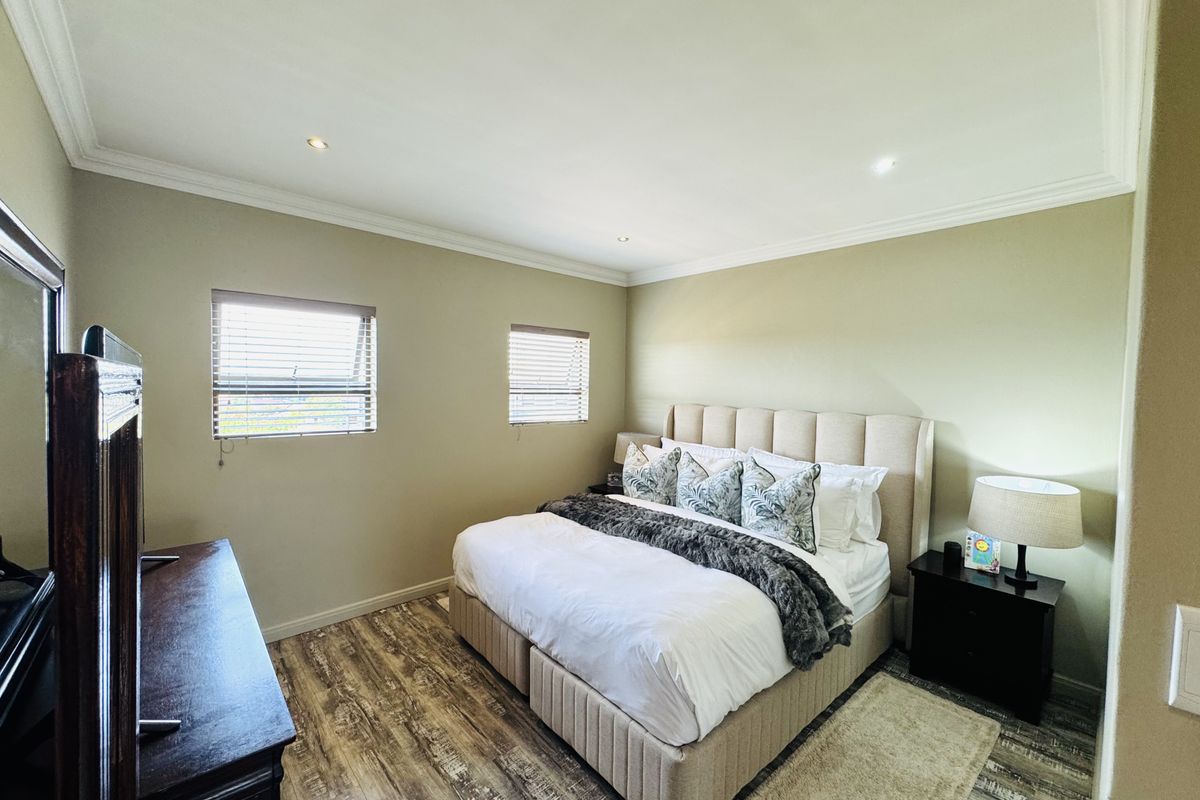 A well-maintained bedroom featuring wood-look flooring, crown molding, and dual windows with fitted blinds.