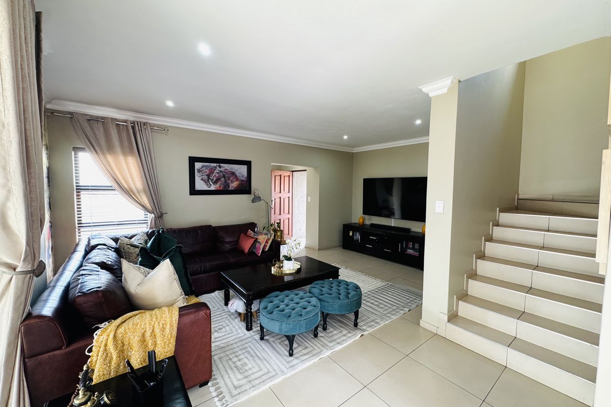 A spacious living room featuring tiled flooring, recessed ceiling lighting, crown molding, and an integrated staircase leading to the upper level.