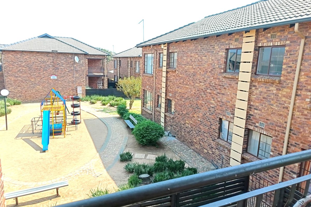 View of a communal apartment complex courtyard featuring face-brick buildings, paved pathways, and a children's playground area.