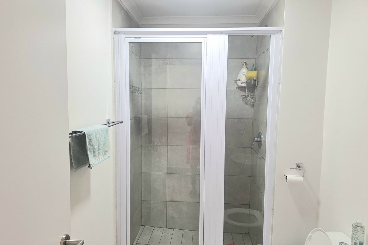 A clean, functional bathroom featuring a glass-enclosed shower with grey wall tiles and a standard toilet.
