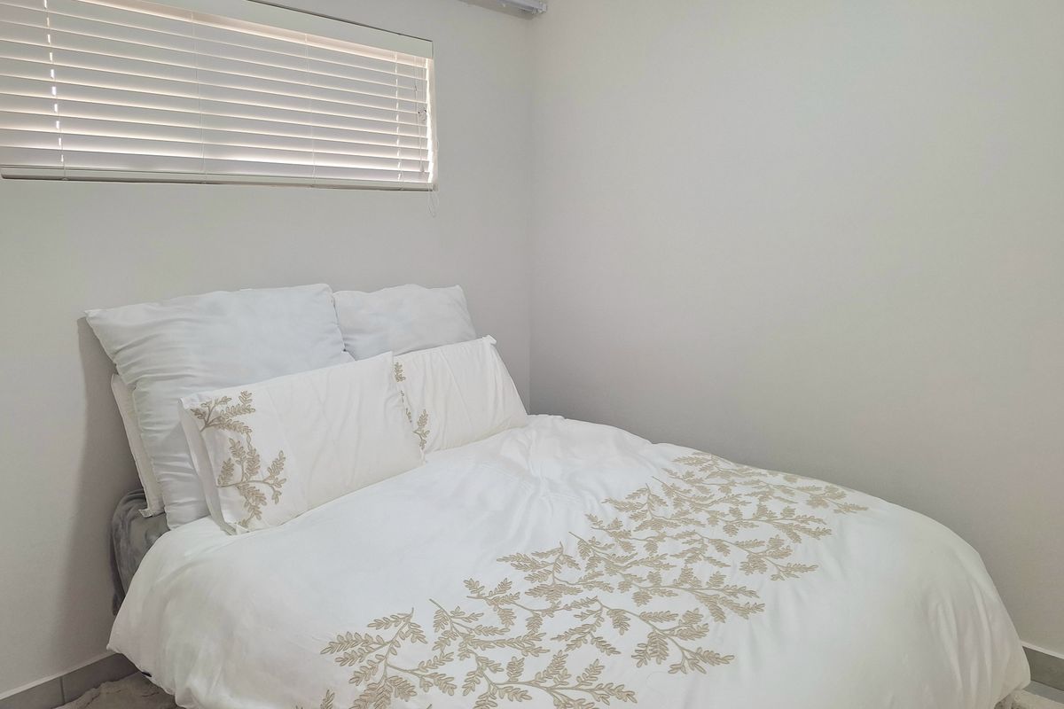 A simple bedroom featuring neutral walls, tiled flooring, and a window fitted with horizontal blinds.