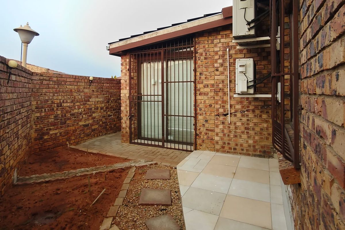 Rear exterior view featuring a paved patio area, face brick walls, security gates, and air conditioning units, with an unfinished garden space.