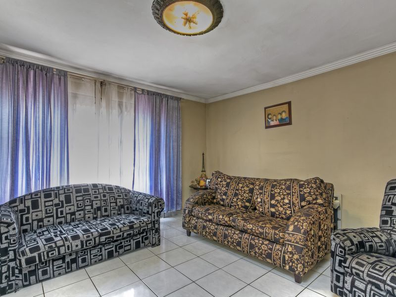 A living room featuring tiled flooring and a ceiling light fixture, currently showing signs of wear on the walls and ceiling.