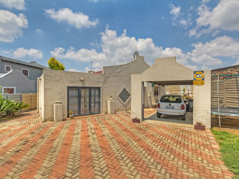 Front elevation of the property featuring a paved driveway, integrated carport, and security gate access.