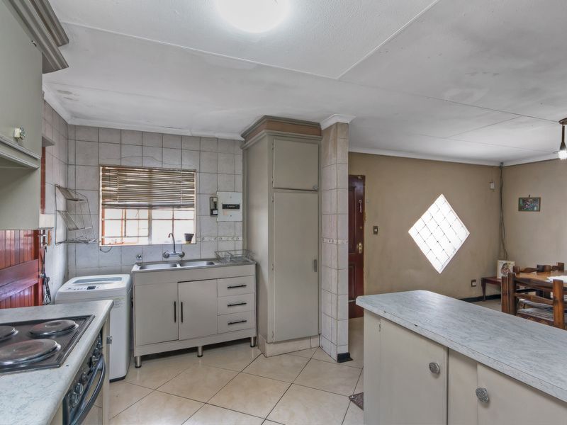 Open-plan kitchen and dining area featuring tiled flooring, built-in cabinetry, electric stove, and a distinctive diamond-shaped glass block window.