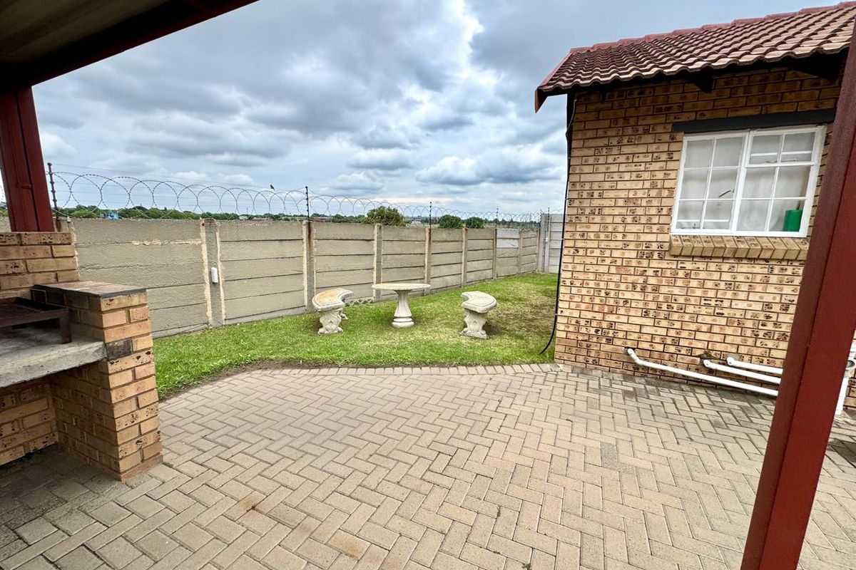 Rear exterior view featuring a paved patio, built-in brick braai, and a private garden enclosed by a precast boundary wall with security fencing.