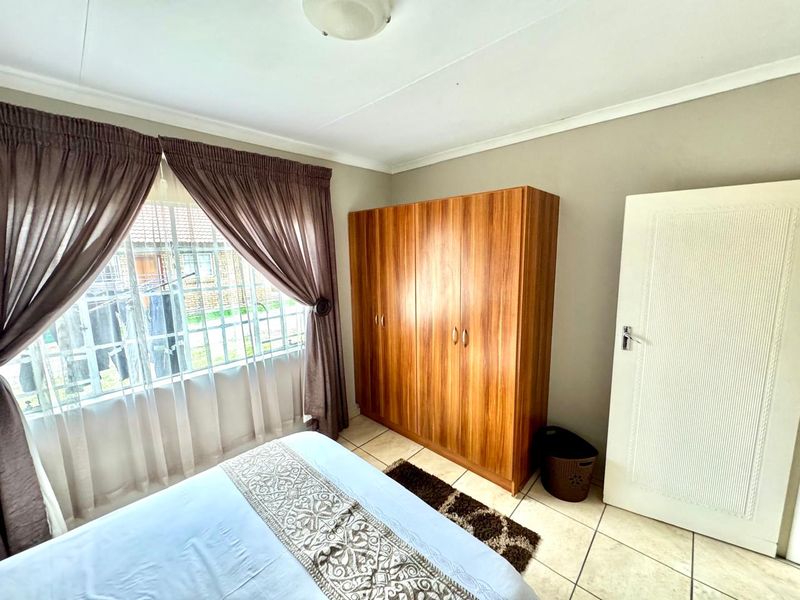 A functional bedroom featuring tiled flooring, a built-in wooden wardrobe, and a window fitted with security bars.