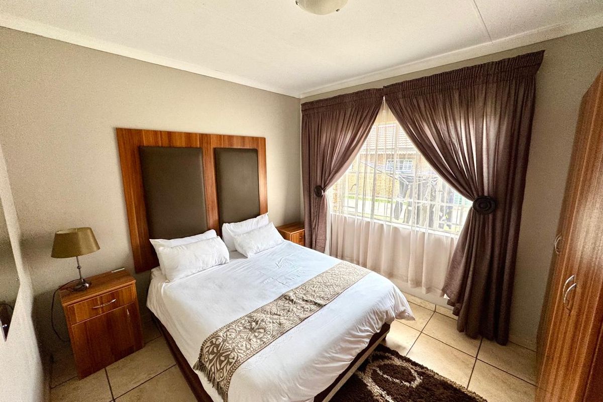 A functional bedroom featuring tiled flooring, a built-in headboard, and a window fitted with security bars for added peace of mind.