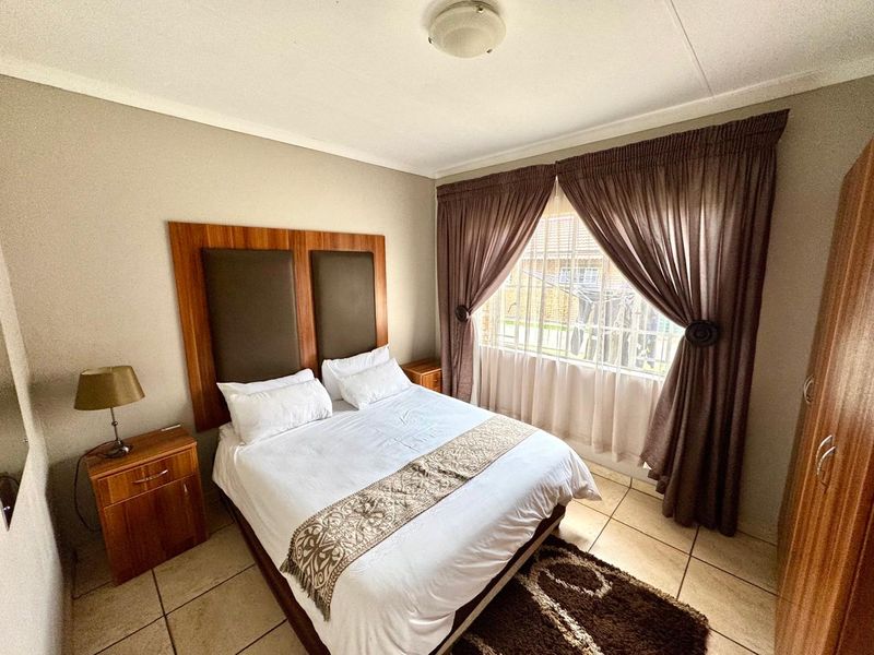 A functional bedroom featuring tiled flooring, a built-in headboard, and a window fitted with security bars for added peace of mind.