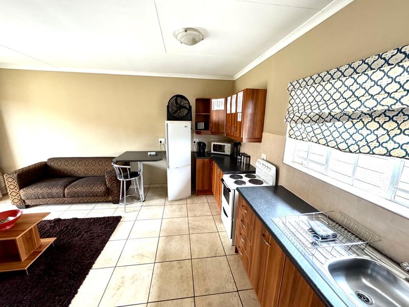 Open-plan living and kitchen area featuring tiled flooring, wood-finish cabinetry, and a functional kitchen layout with a freestanding stove and sink.