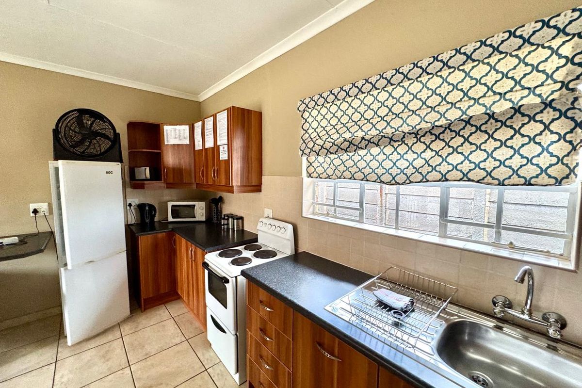 A functional kitchen featuring wood-finish cabinetry, dark laminate countertops, a stainless steel sink, and a freestanding stove with tiled flooring.