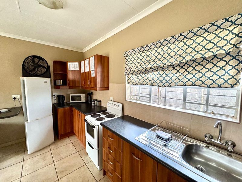 A functional kitchen featuring wood-finish cabinetry, dark laminate countertops, a stainless steel sink, and a freestanding stove with tiled flooring.