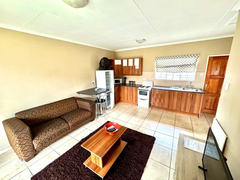 Open-plan living and kitchen area featuring tiled flooring, wooden cabinetry, and a functional layout suitable for modern updates.