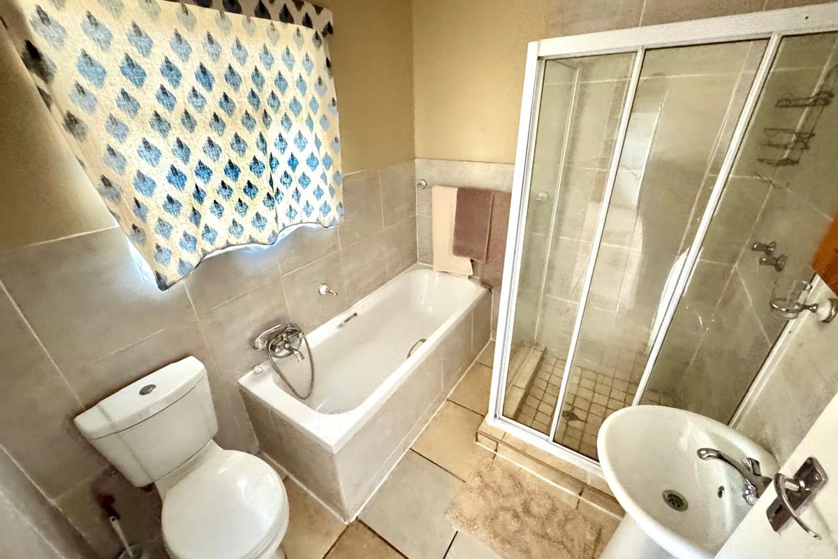 A functional bathroom featuring a bathtub, separate shower enclosure, pedestal sink, and toilet with neutral wall and floor tiling.