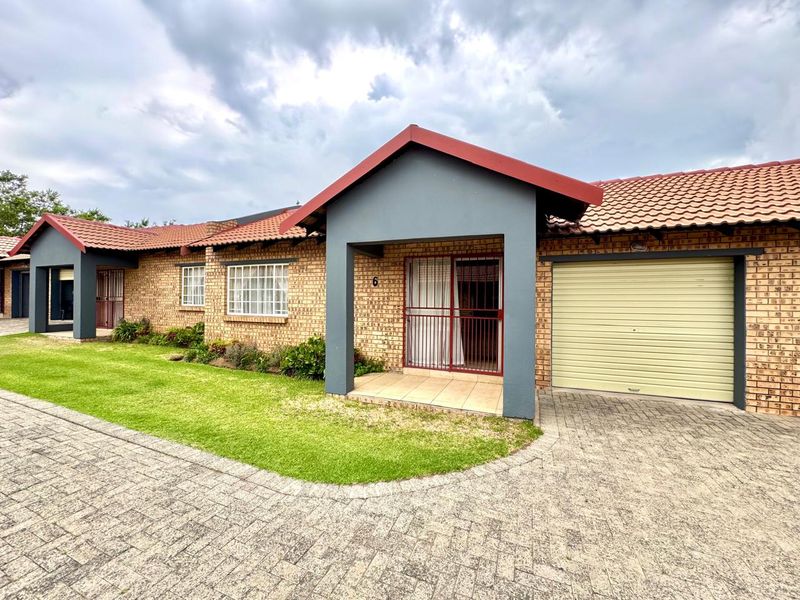 Front elevation of a face brick townhouse featuring a tiled roof, a single roll-up garage door, and a paved driveway with a small garden area.