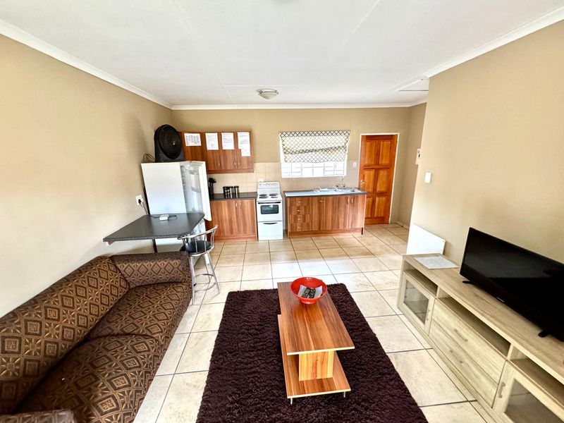 Open-plan living area featuring a functional kitchen with wood-finish cabinetry, tiled flooring, and direct access to the exterior.