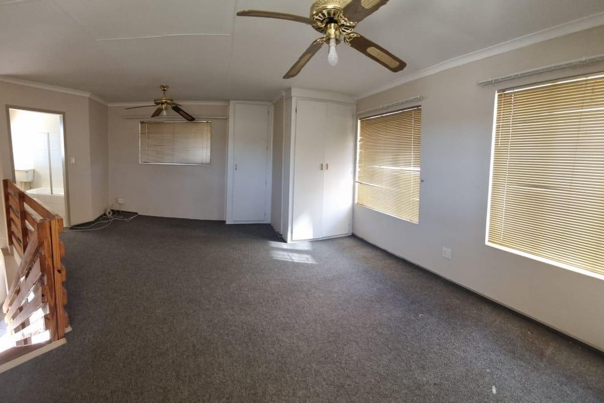 Spacious bedroom featuring built-in cupboards, carpeted flooring, and dual ceiling fans, with an adjacent staircase leading to the lower level.