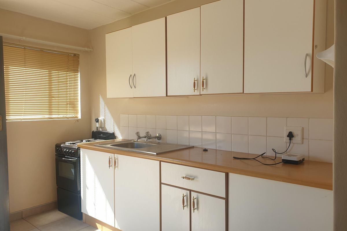 A functional kitchen featuring white cabinetry, a stainless steel sink, tiled backsplash, and a freestanding stove, offering a clean and practical workspace.