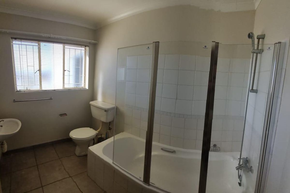 A functional bathroom featuring a bathtub with a glass shower screen, a toilet, and a wall-mounted basin with tiled flooring.