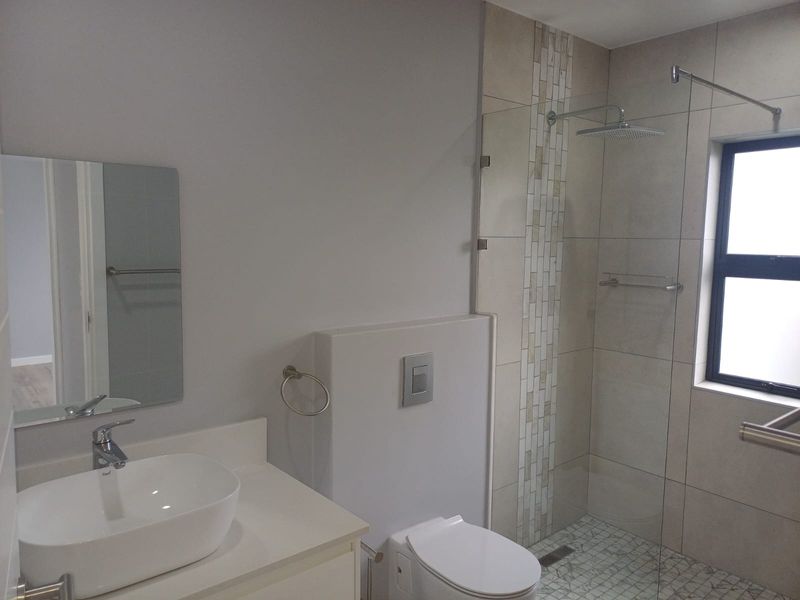 Modern bathroom featuring a vessel sink, concealed cistern toilet, and a spacious walk-in shower with a rain shower head and mosaic tile flooring.