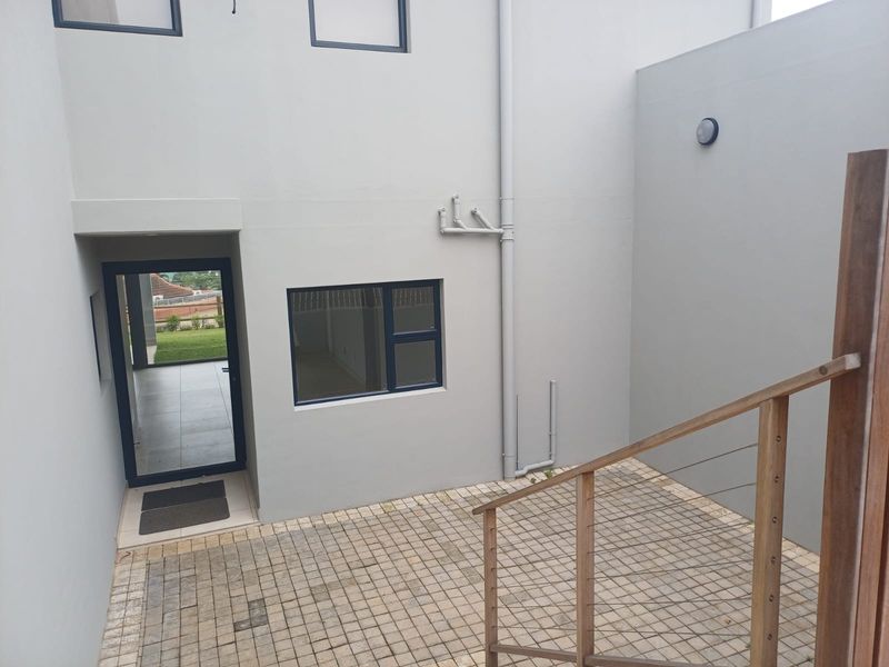 A clean, paved rear courtyard featuring a timber and wire balustrade, external plumbing, and modern aluminium window and door frames.