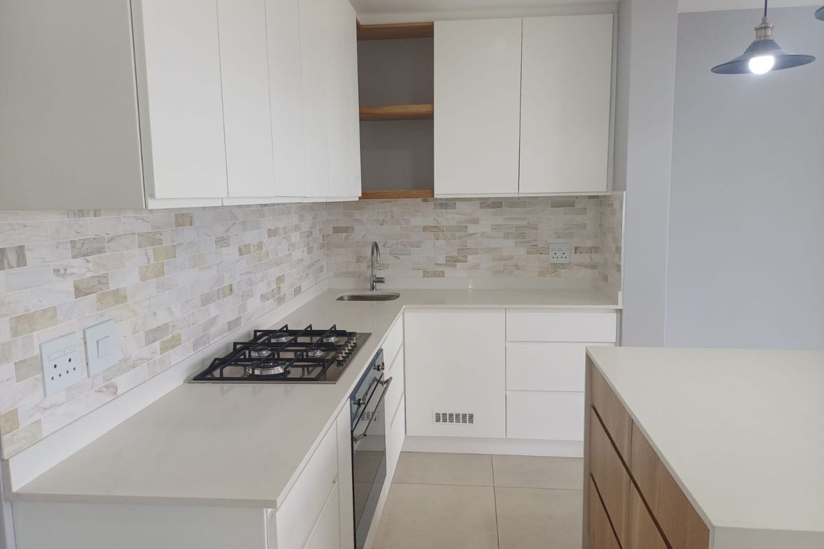 Modern kitchen featuring white cabinetry, stone countertops, gas hob, built-in oven, and a stylish tiled backsplash in a clean, contemporary finish.