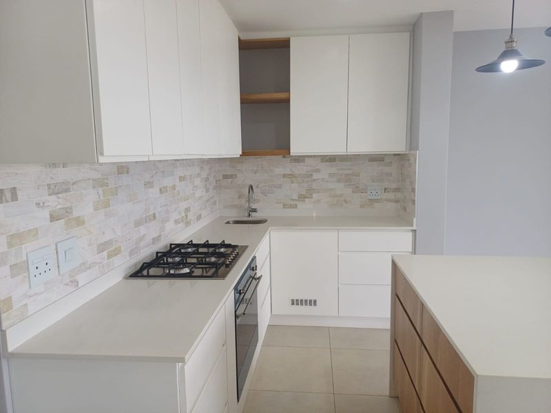 Modern kitchen featuring white cabinetry, stone countertops, gas hob, built-in oven, and a stylish tiled backsplash in a clean, contemporary finish.