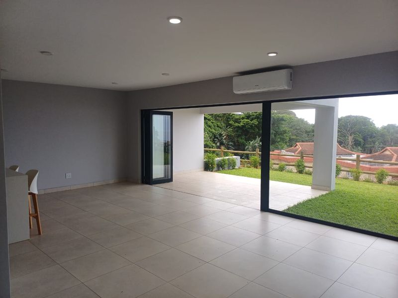 Spacious open-plan living area featuring large format floor tiles, recessed lighting, and expansive sliding doors that open onto a covered patio and garden.