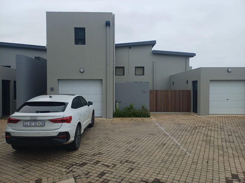 Modern residential facade featuring double garages, paved driveway, and contemporary grey exterior finishes with timber gate detailing.