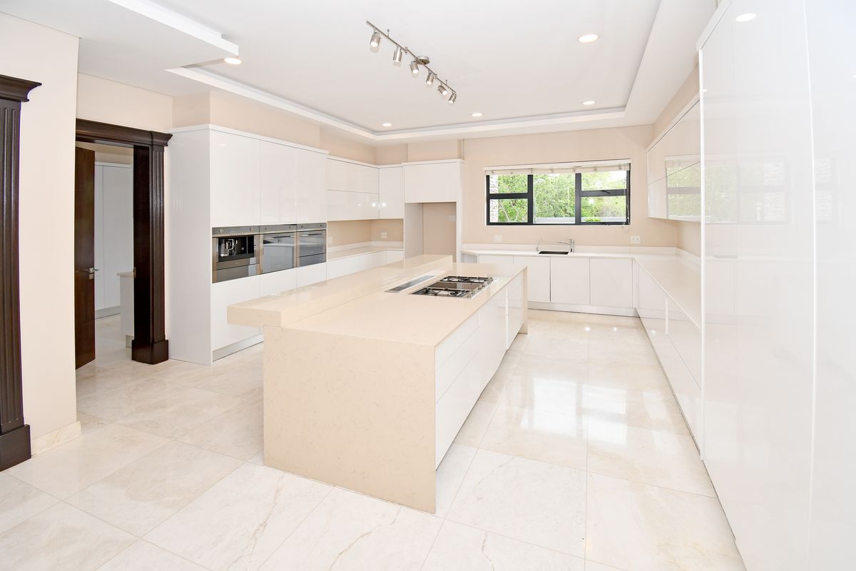 Modern kitchen featuring high-gloss white cabinetry, a large central island with integrated gas hob, stone countertops, and polished marble-style floor tiles.