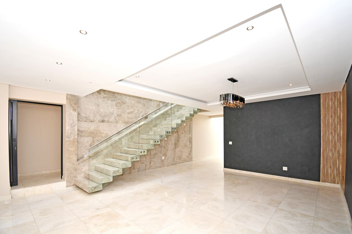 Modern open-plan living area featuring a striking floating staircase with glass balustrades, marble-tiled flooring, and a feature wall with timber slat detailing.
