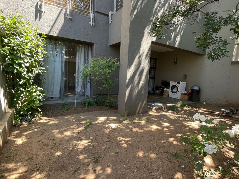 A rear exterior view of the apartment featuring a covered patio area and a small private garden space with boundary walls.