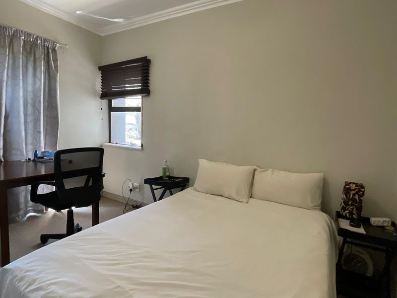 A functional bedroom featuring carpeted flooring, a sliding glass door providing natural light, and a window with fitted wooden blinds.