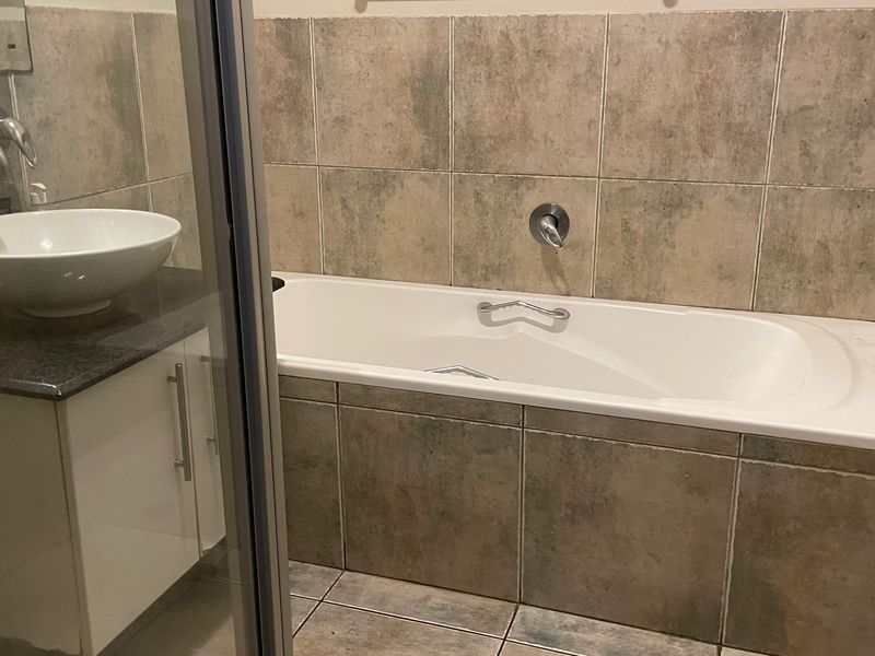A functional bathroom featuring a built-in bathtub, a modern vessel sink vanity with wall-mounted tapware, and neutral tiled finishes throughout.