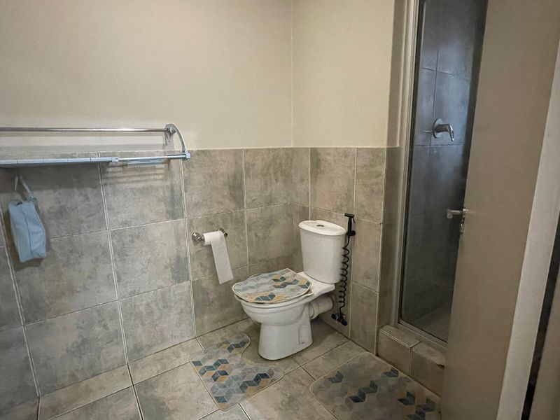 A functional bathroom featuring a toilet, a glass-enclosed shower, and neutral-toned wall and floor tiling.