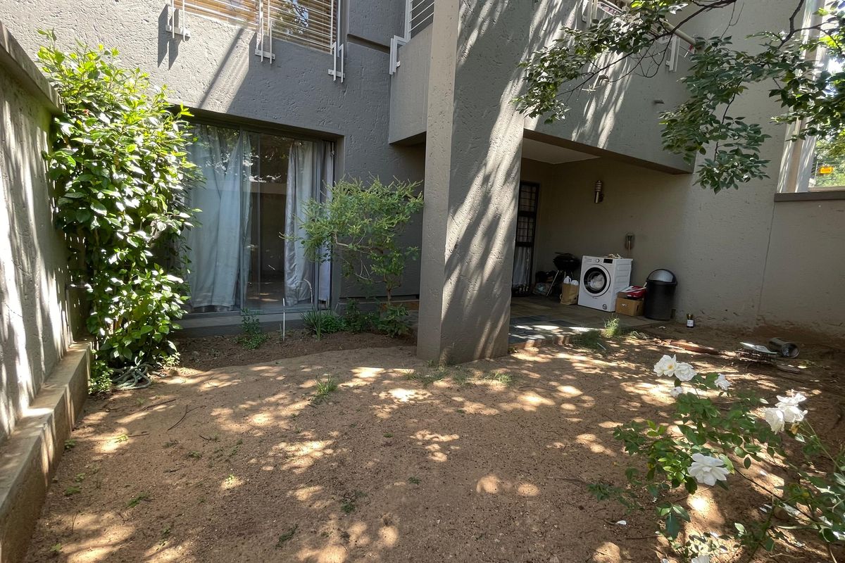 A rear exterior view of the apartment featuring a covered patio area and a small private garden space with boundary walls.