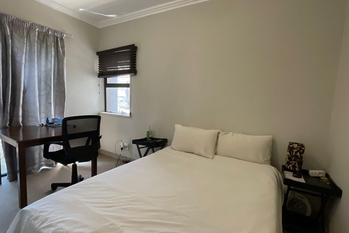 A functional bedroom featuring carpeted flooring, a sliding glass door providing natural light, and a window with fitted wooden blinds.