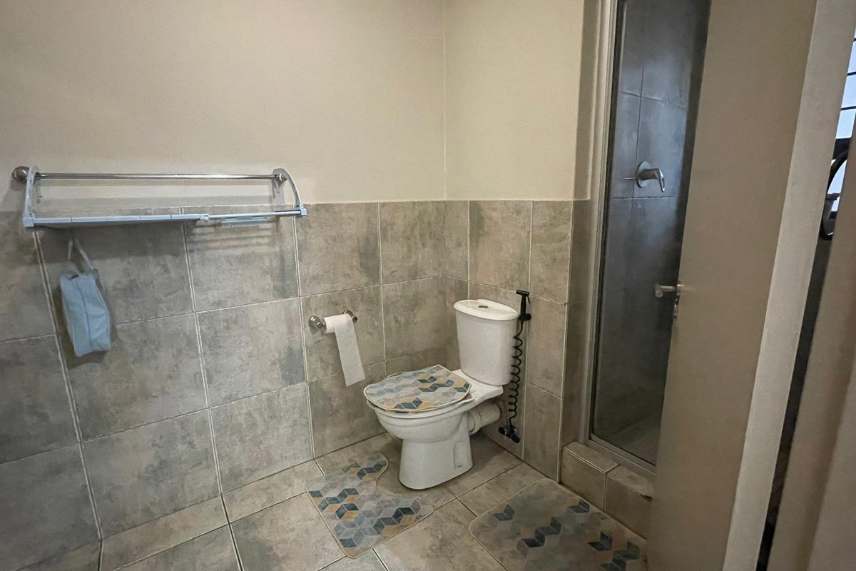 A functional bathroom featuring a toilet, a glass-enclosed shower, and neutral-toned wall and floor tiling.