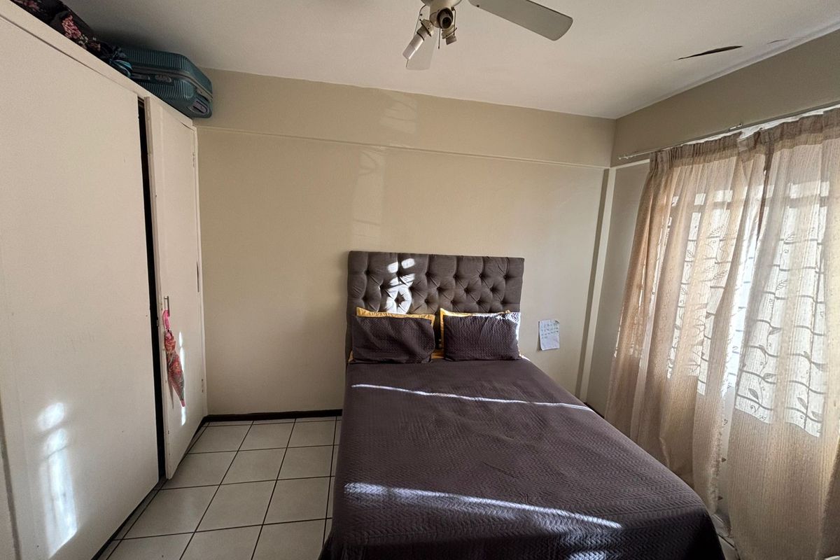 A bedroom featuring tiled flooring, a built-in wardrobe, and a ceiling fan. The room requires minor ceiling repairs.