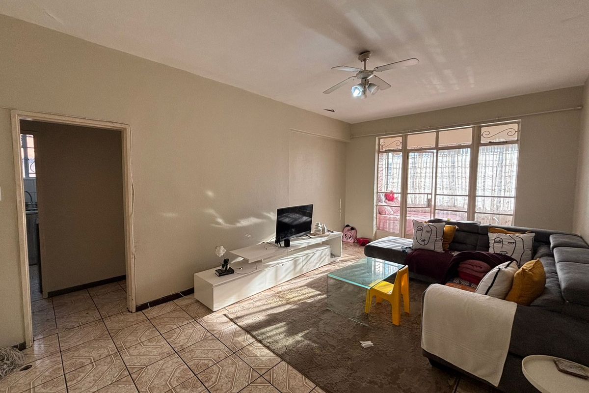 A spacious living room featuring tiled flooring, a ceiling fan, and large windows that provide ample natural light.