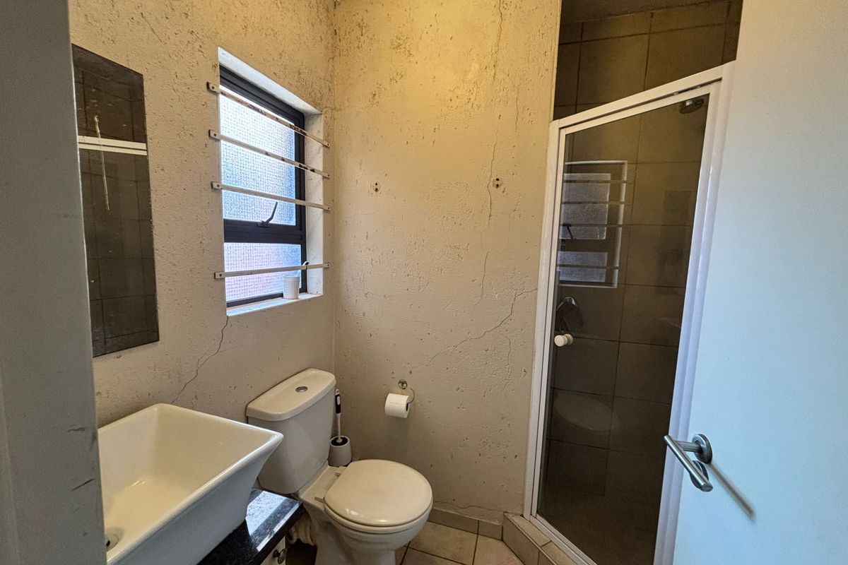 A compact bathroom featuring a shower enclosure, toilet, and basin, requiring cosmetic updates to the wall finishes and ceiling.