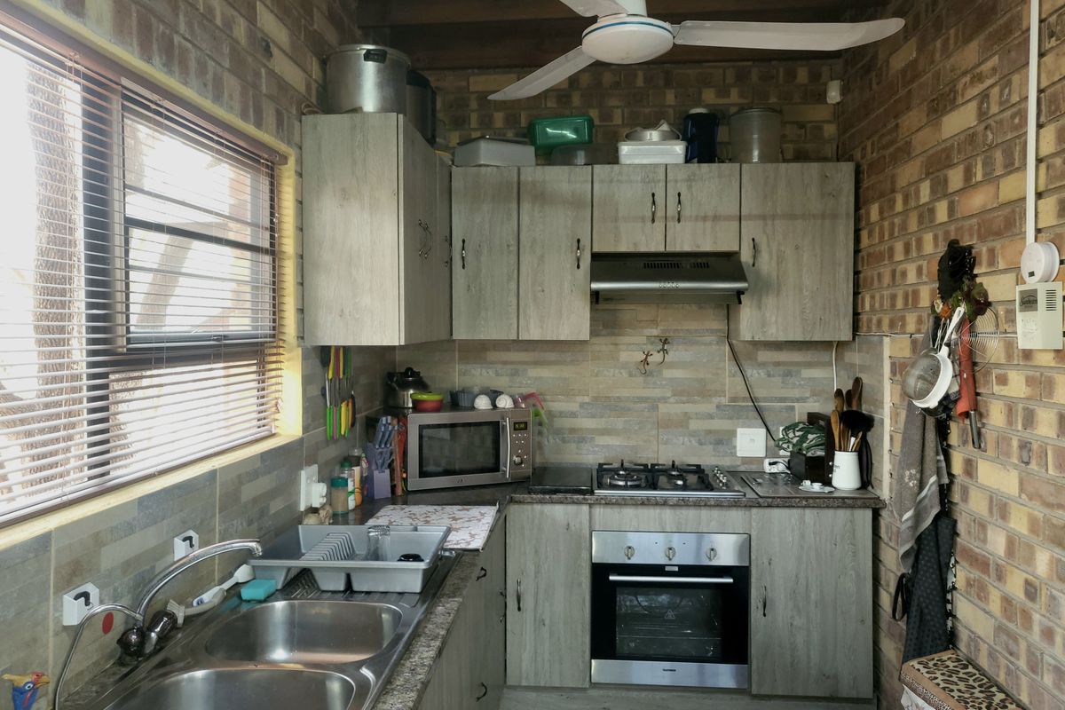 Compact kitchen featuring exposed brick walls, wood-look cabinetry, built-in oven with gas hob, and a double bowl stainless steel sink.