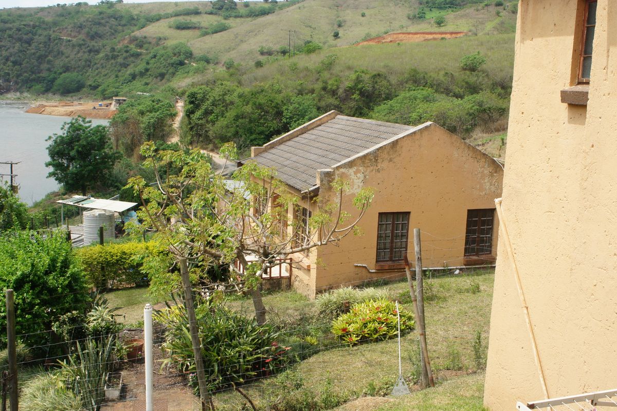 Elevated view of a rural farm property featuring a detached dwelling with a tiled roof, set against a scenic river and hillside landscape.